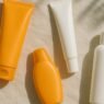 A flat lay of assorted sunscreen tubes, bottles and sticks arranged on a pastel surface